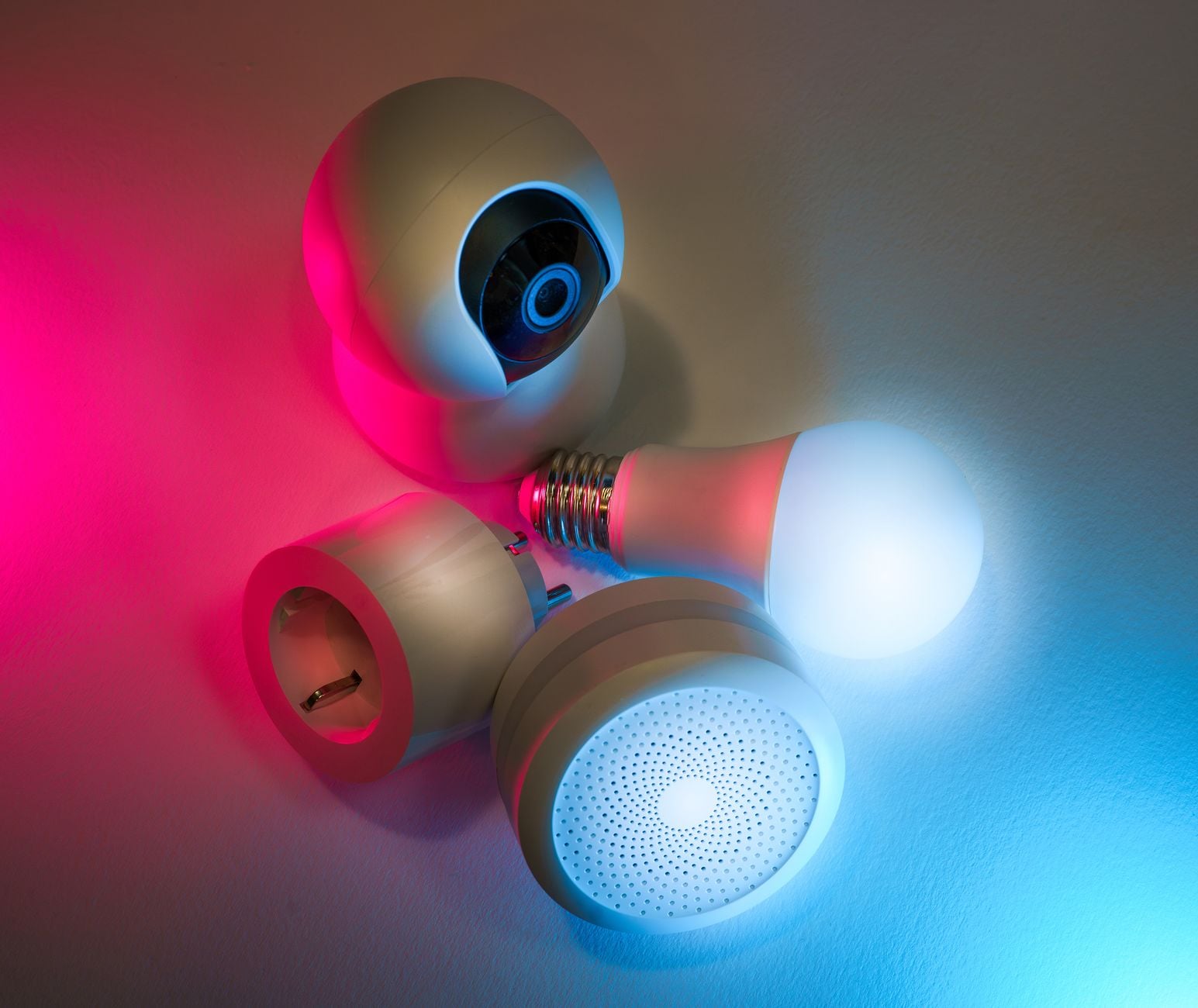 Cámara de vigilancia, bombilla inteligente, altavoz y sensor de humo con iluminación rosa y azul sobre fondo gradiente
