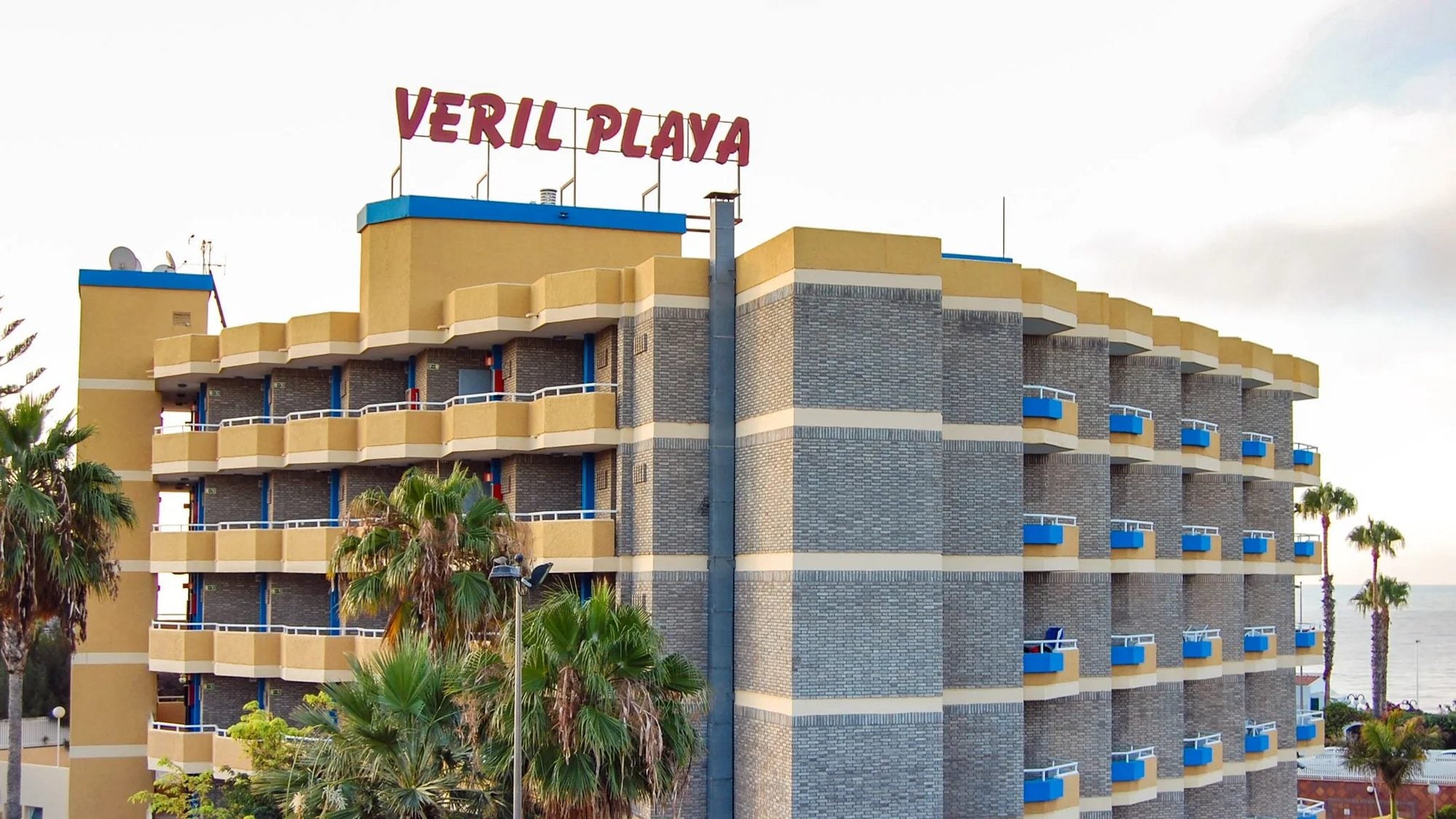 Hotel Veril Playa con fachada amarilla y azul rodeado de palmeras