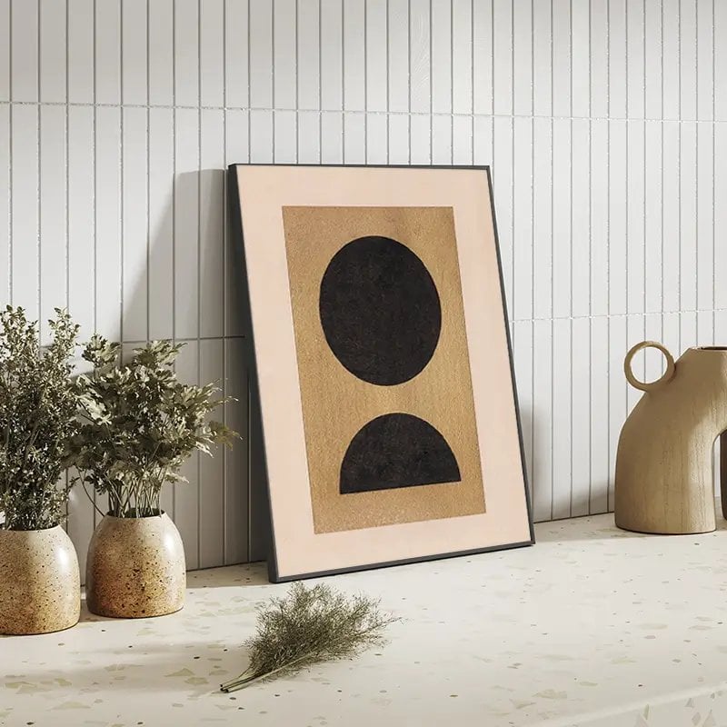 Composition minimaliste avec poster encadré aux formes géométriques noires, vases dorés et plantes séchées