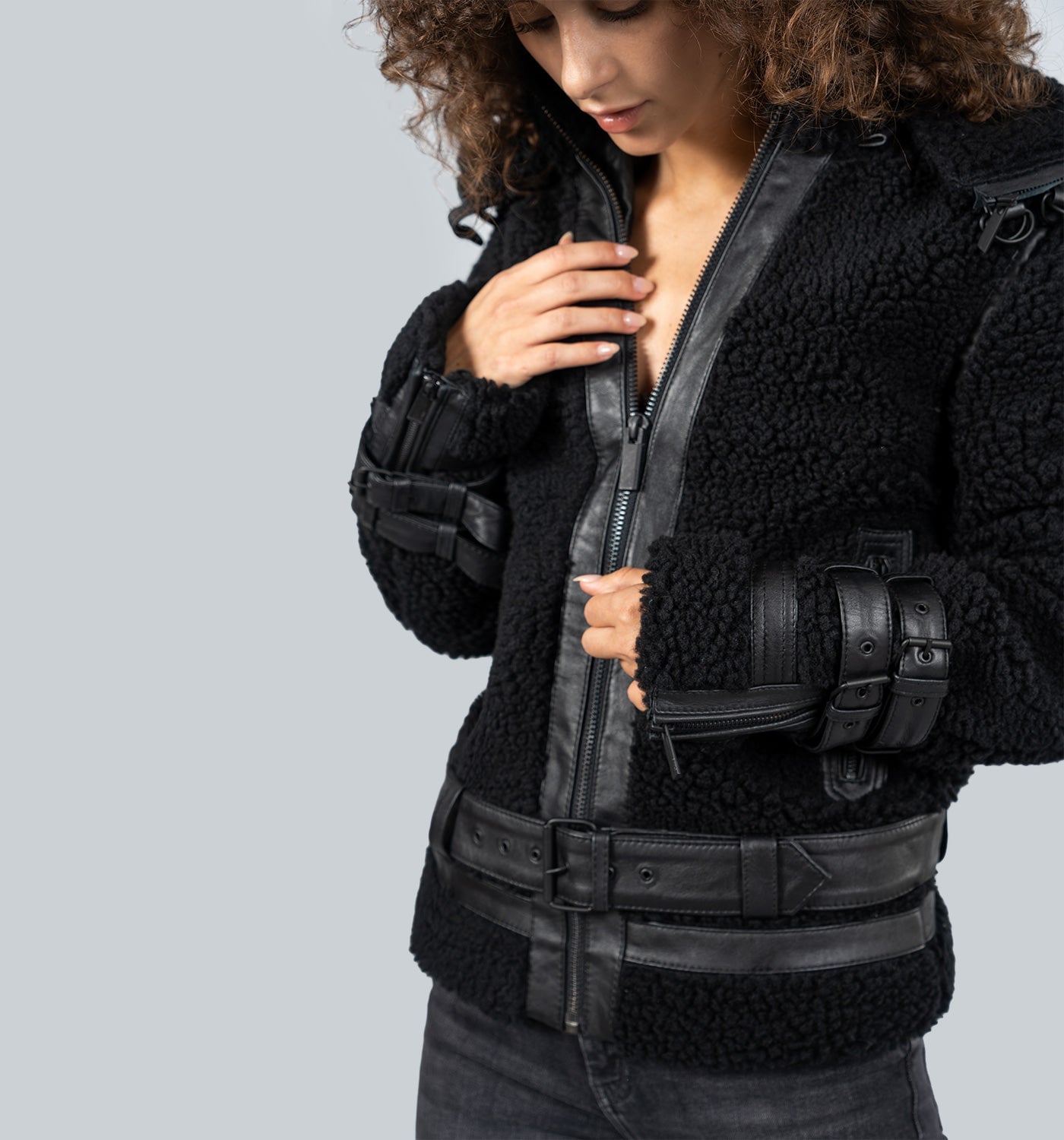 Mädchen mit lockigem braunem Haar in schwarzer Lederjacke mit Reißverschluss und Gürtel