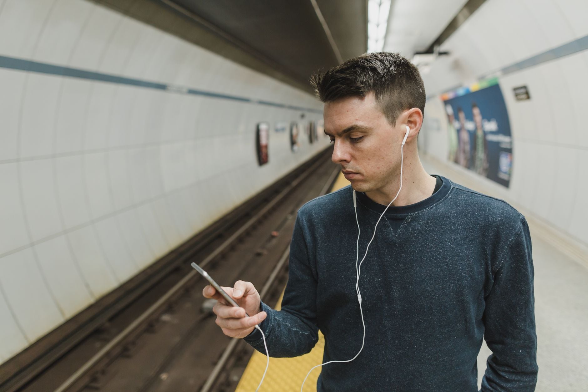 Junger Mann mit Kopfhörern schaut auf sein Smartphone in einer U-Bahn-Station