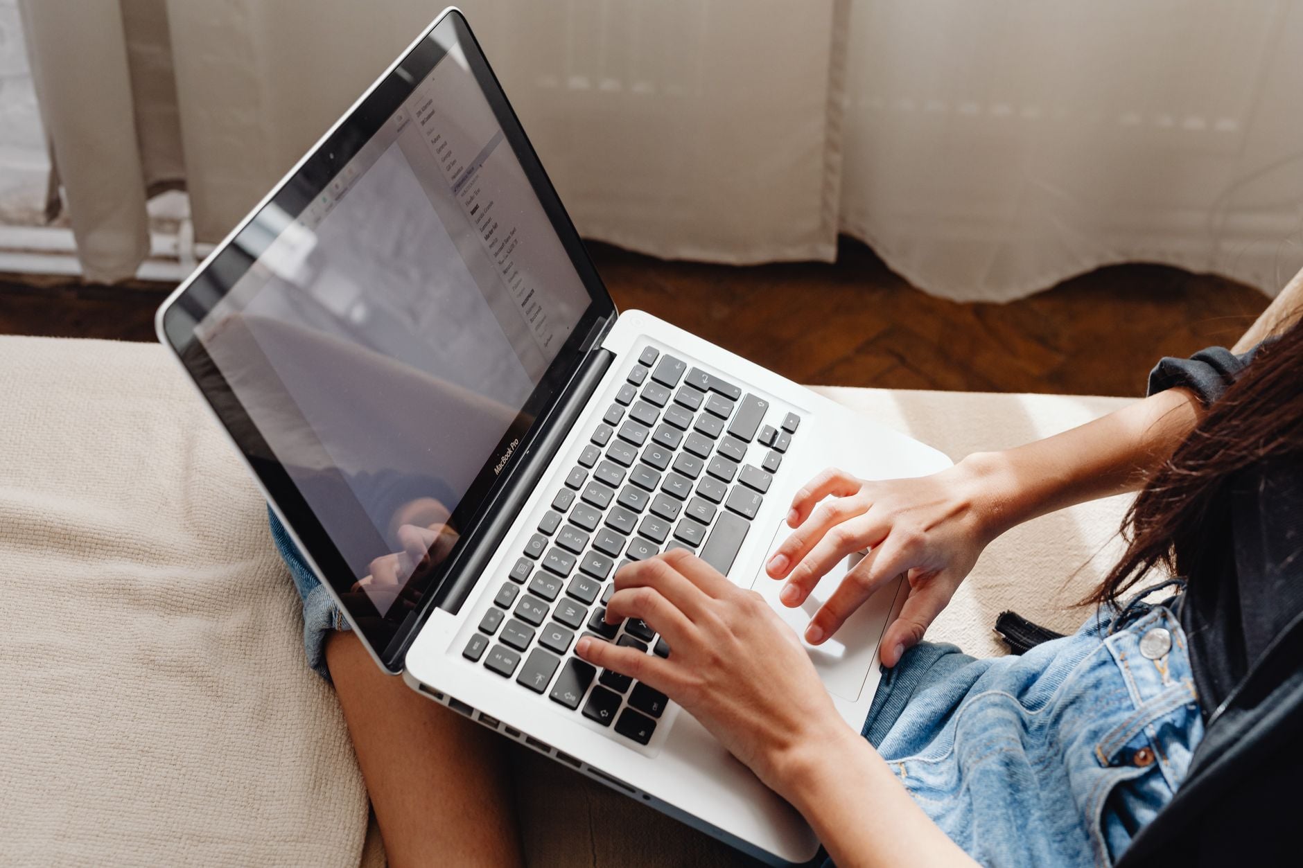 Person's hands typing on a laptop while sitting on a couch