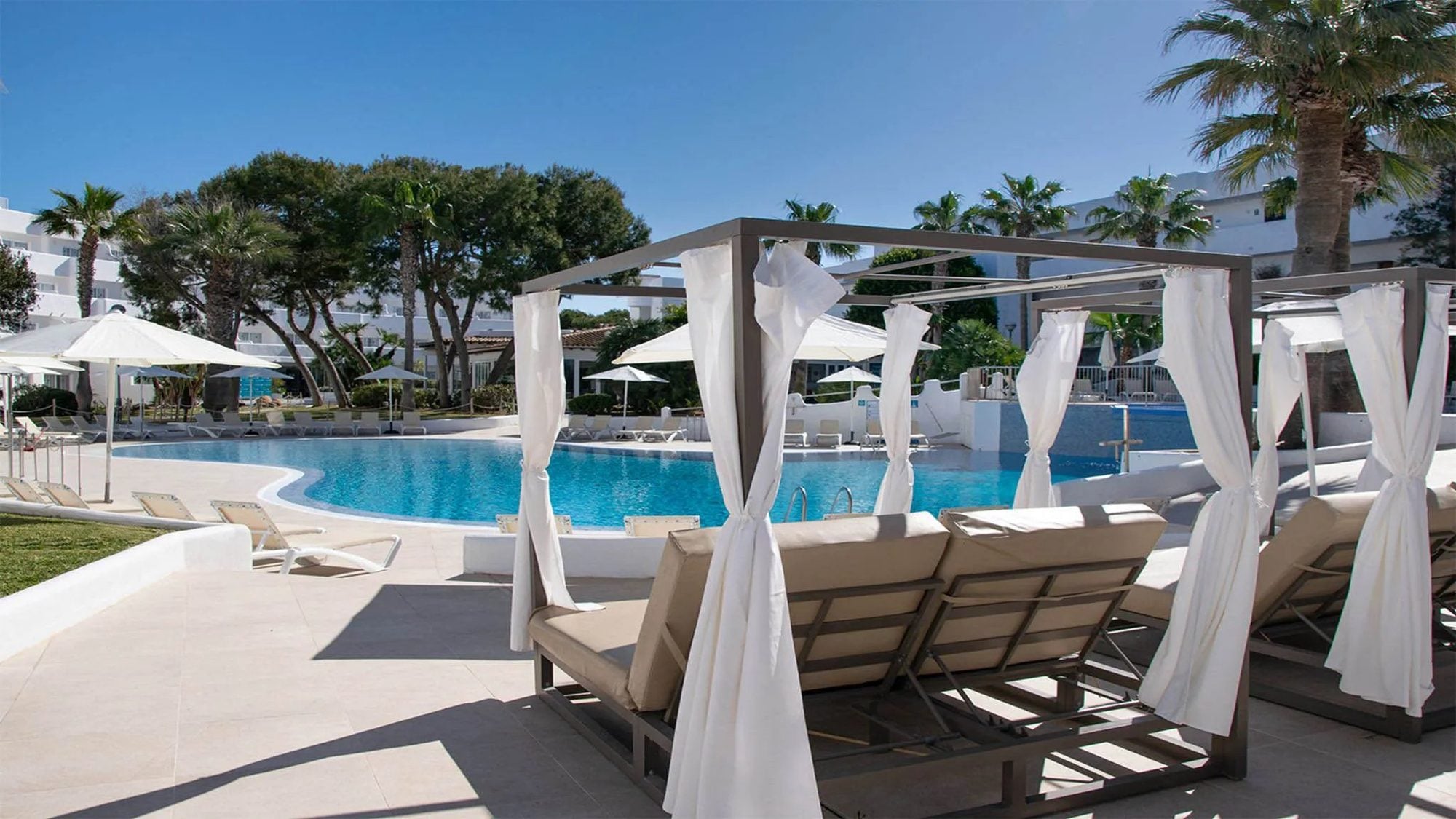 Área de piscina con camastros bajo pérgolas blancas y sombrillas