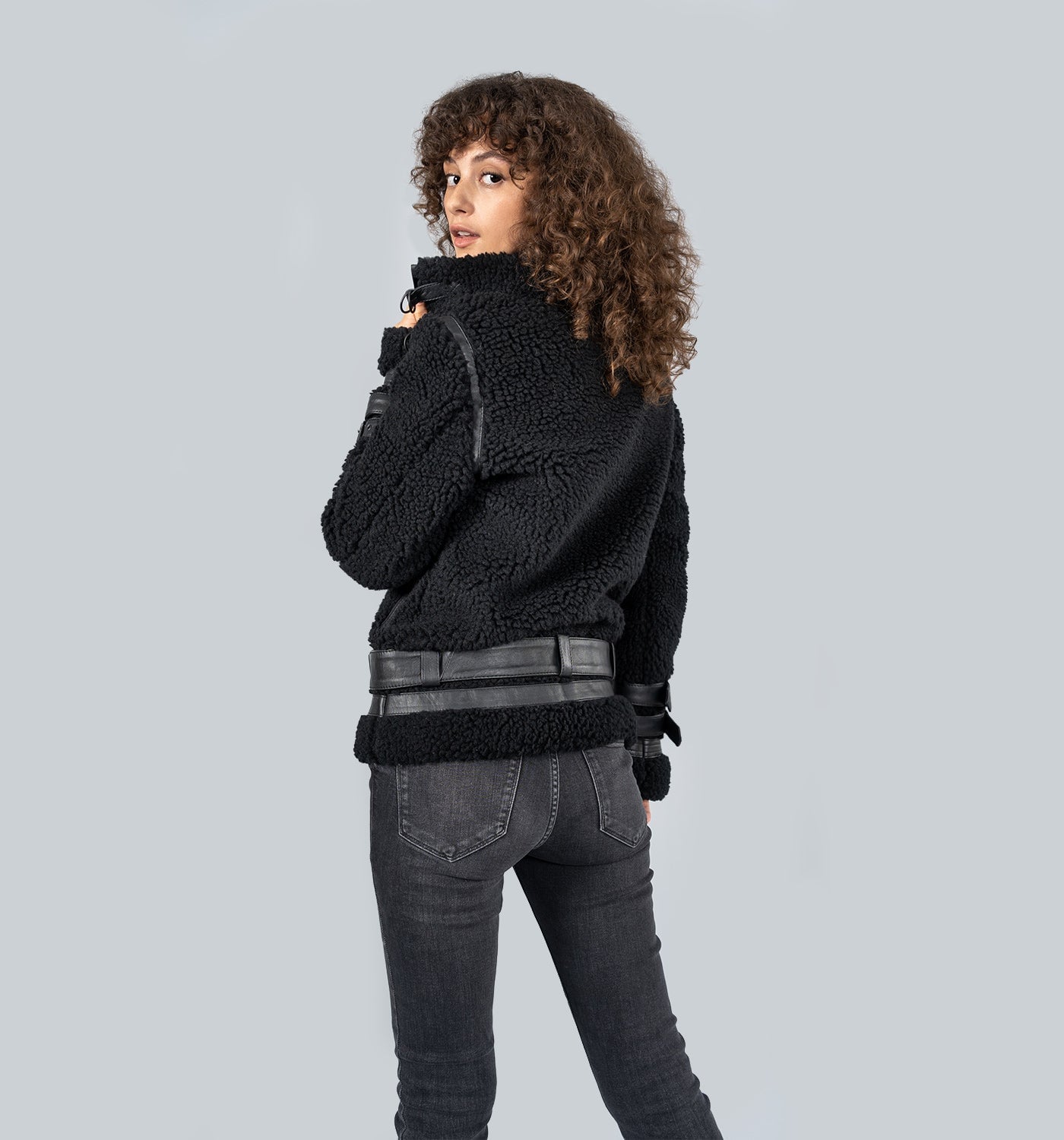 Mädchen von hinten in schwarzer Fleece-Jacke mit grauem Gürtel und dunkler Jeans