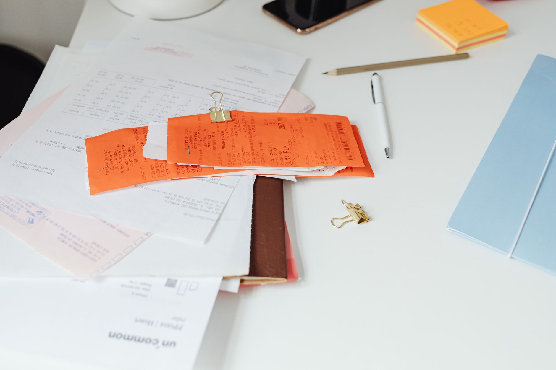 Skrivbord med orange märkta dokument fästa med binder, omgivna av anteckningsblock och penna
