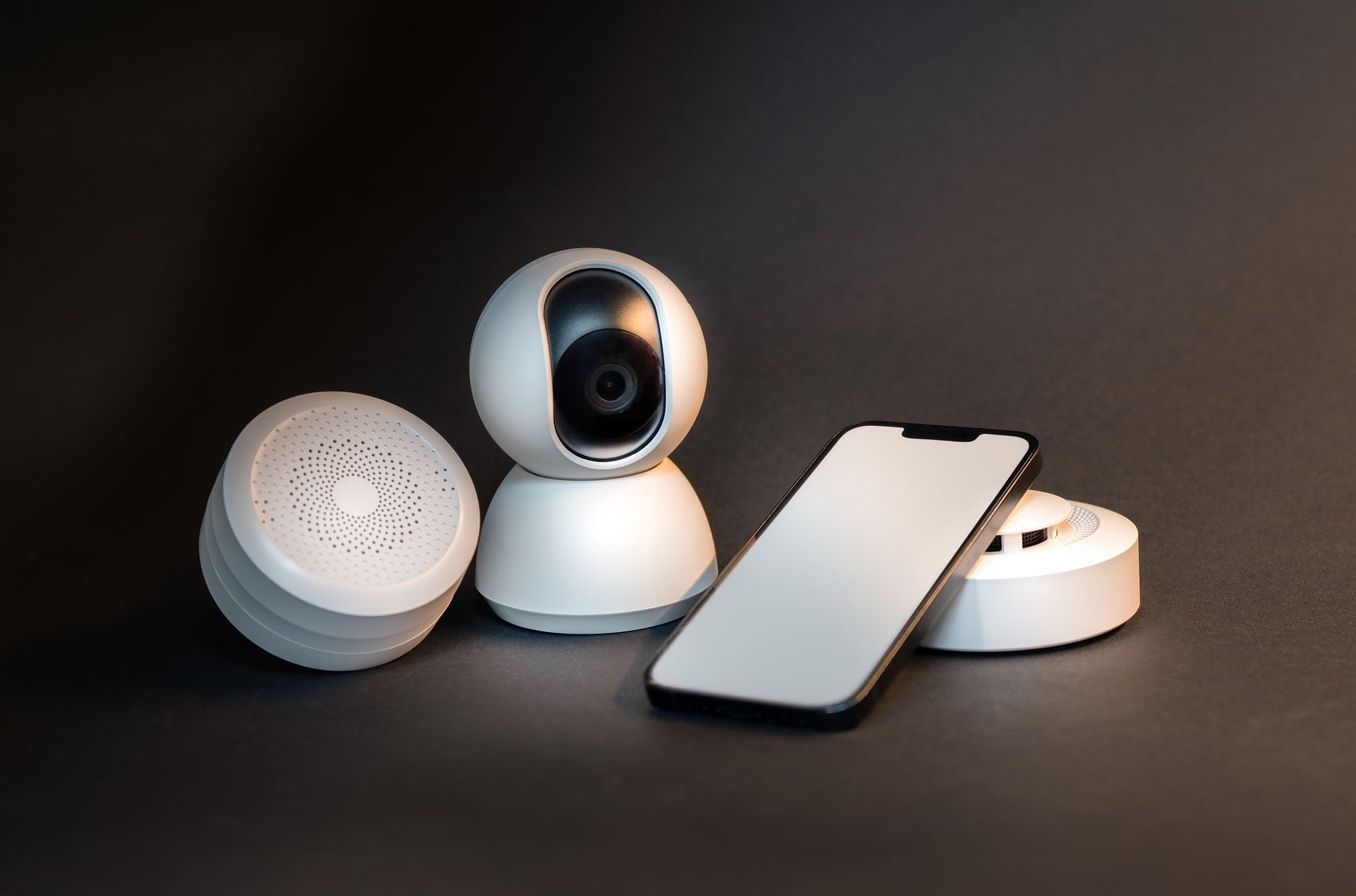 Dispositivos de hogar inteligente incluyendo altavoz, cámara de seguridad, sensor de humo y smartphone sobre fondo oscuro