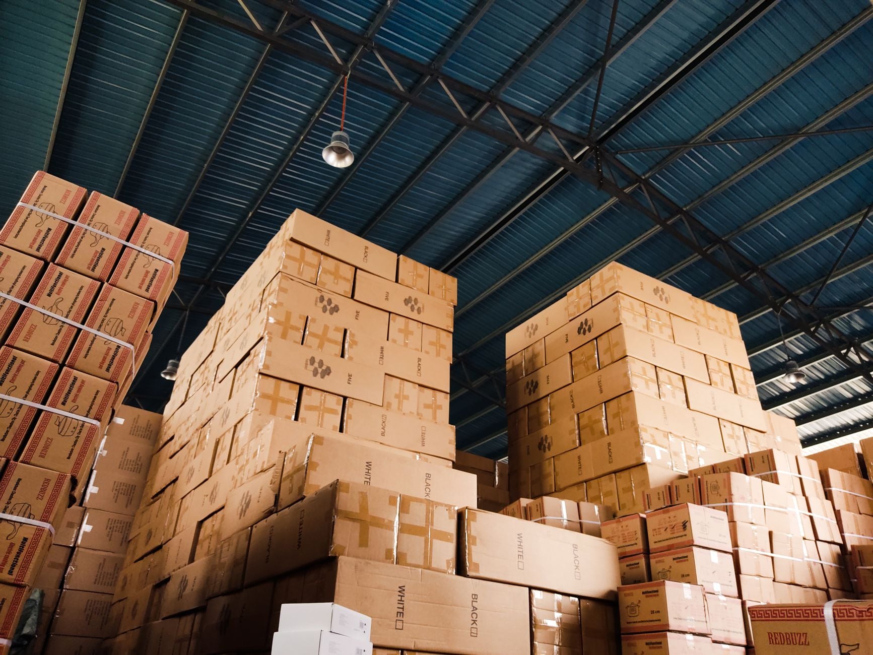 Entrepôt avec des palettes de cartons de différentes tailles et formats stockés sous un toit métallique