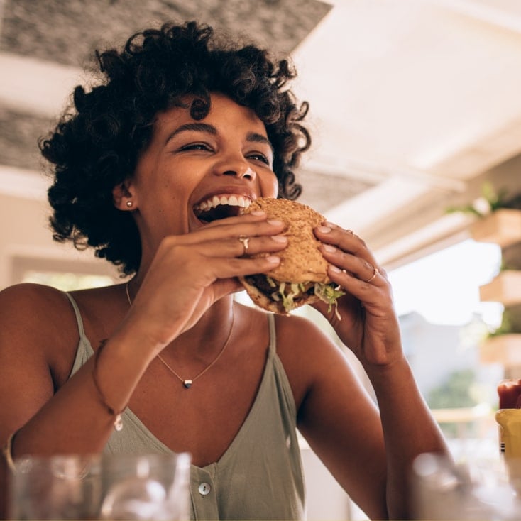 Mujer sonriendo mientras come un sándwich en un restaurante al aire libre