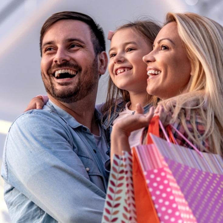 Familia de tres personas sonriendo juntas en un día soleado al aire libre